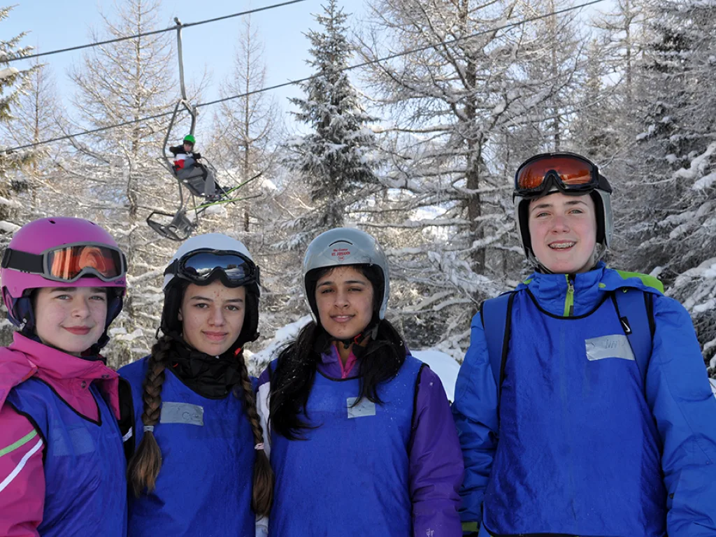 Vier Jugendliche mit Helm und Skibrille vor dem verschneiten Wald.